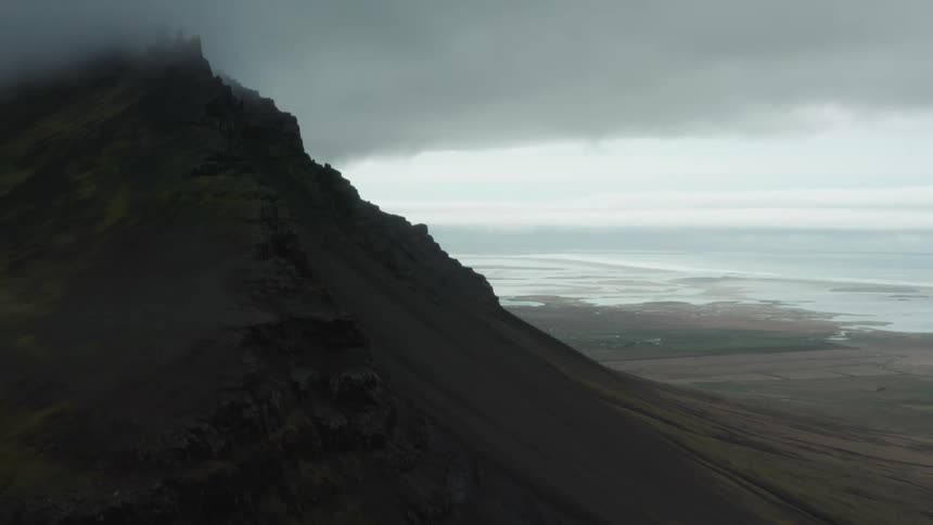 Aerial view of the barren slopes of a mountain next to the ocean