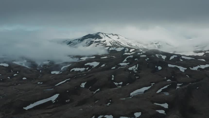 A large mountain that is covered in snow is surrounded by a desolate landscape