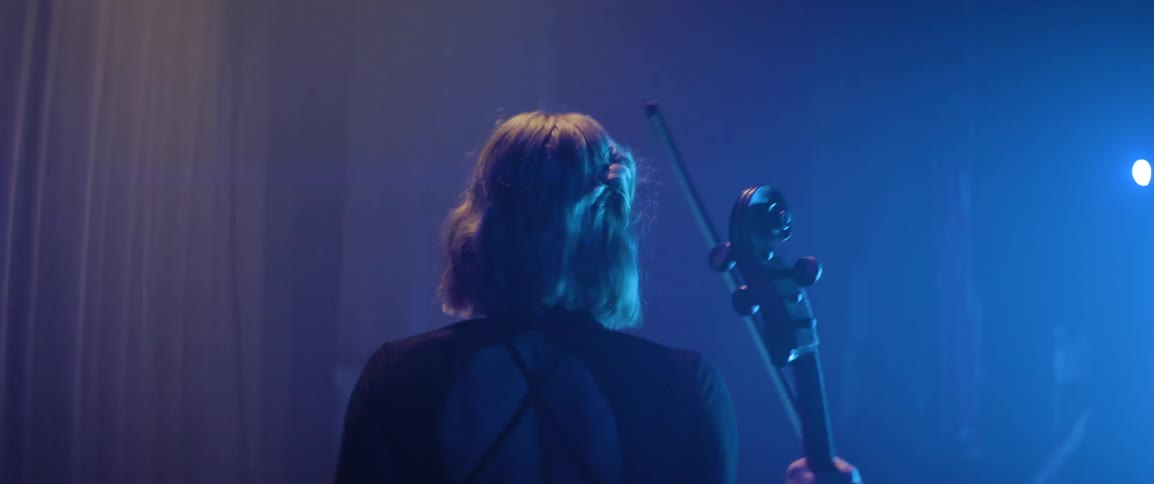 Cello performer begins walking from the theater wings towards the stage with her instrument