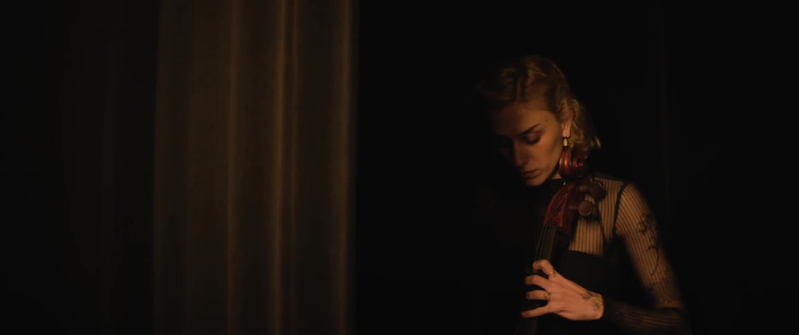 A woman practises cello behind a stage curtain