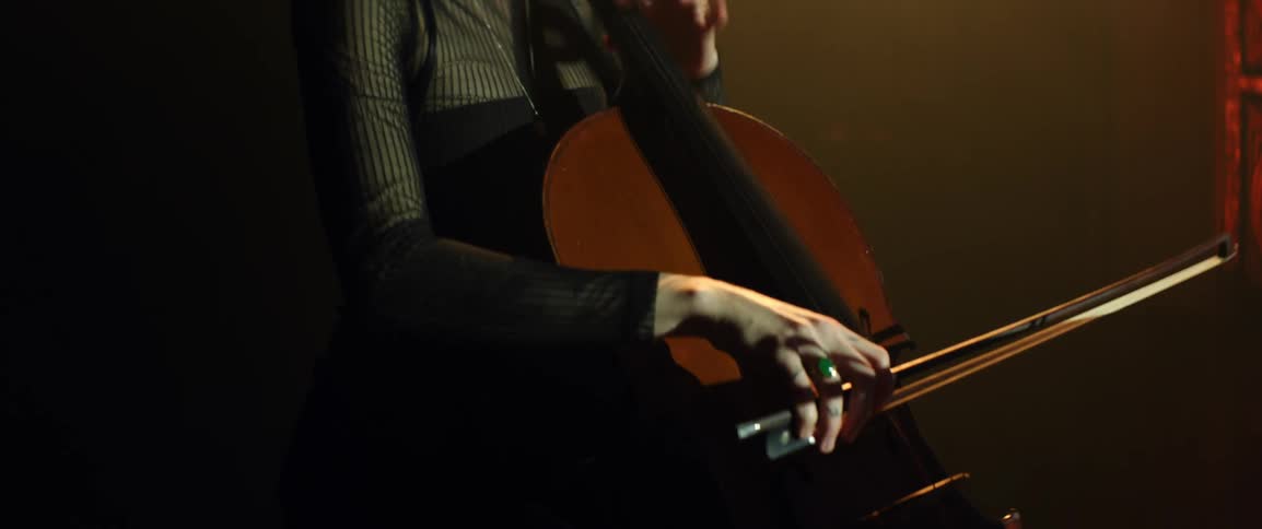 A woman is playing the cello under a golden spotlight