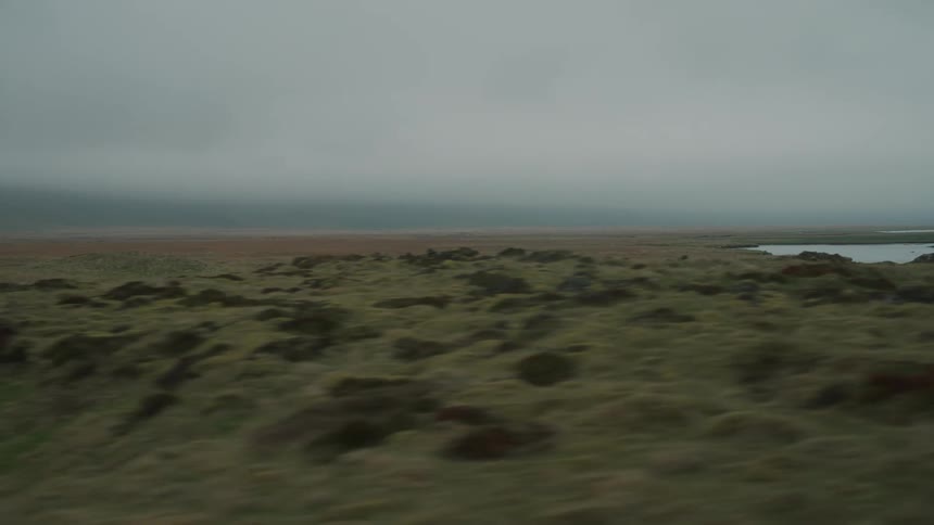 Car driving close to a beach coast with rocky plain during a cloudy day