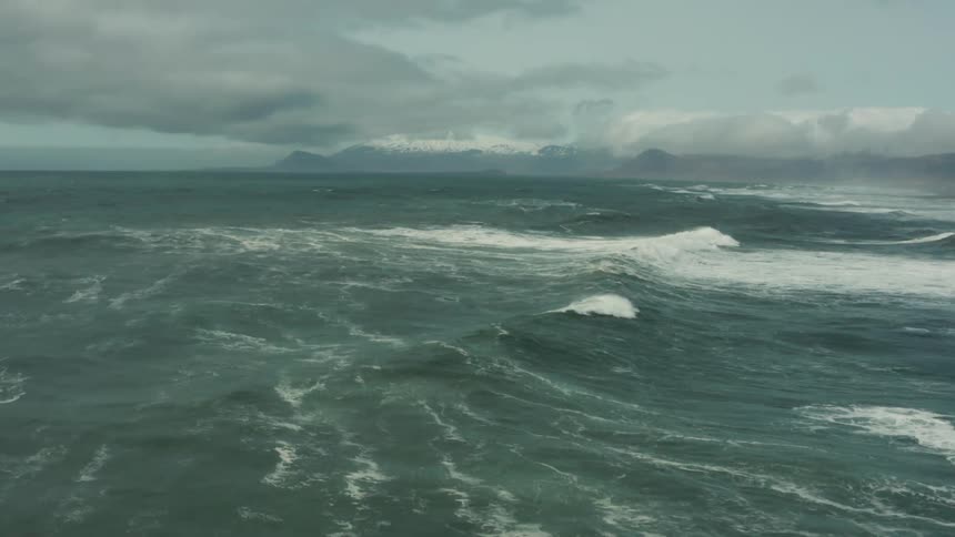 Waves curl and splash as they roll into shore under a cloudy sky