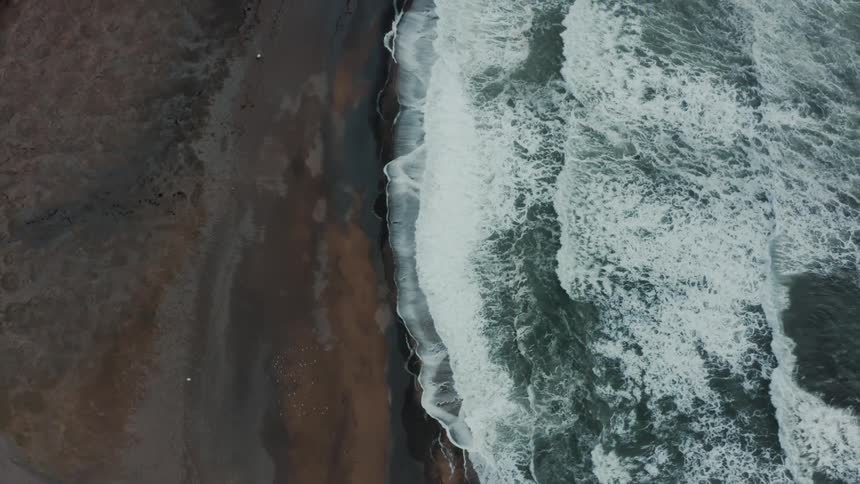 Aerial view of waves rolling into shore and over the beach