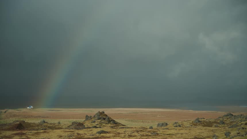 A rainbow glows near a rural house across the sky and open land