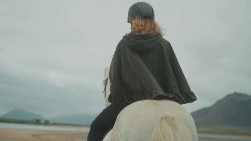 A person riding a horse on the beach during a cloudy day