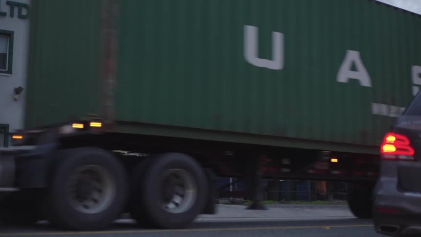 Cars passing through a street and a truck with a green container also passes by