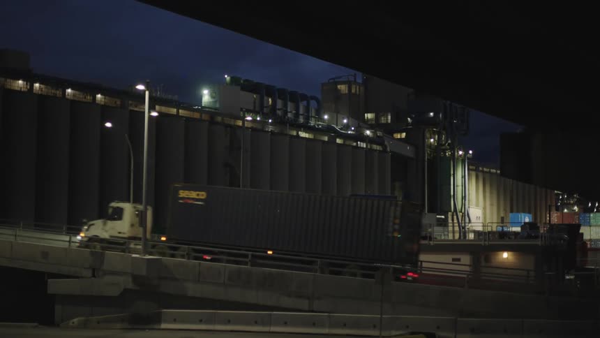 Truck drives in front of an industrial building with silos at night