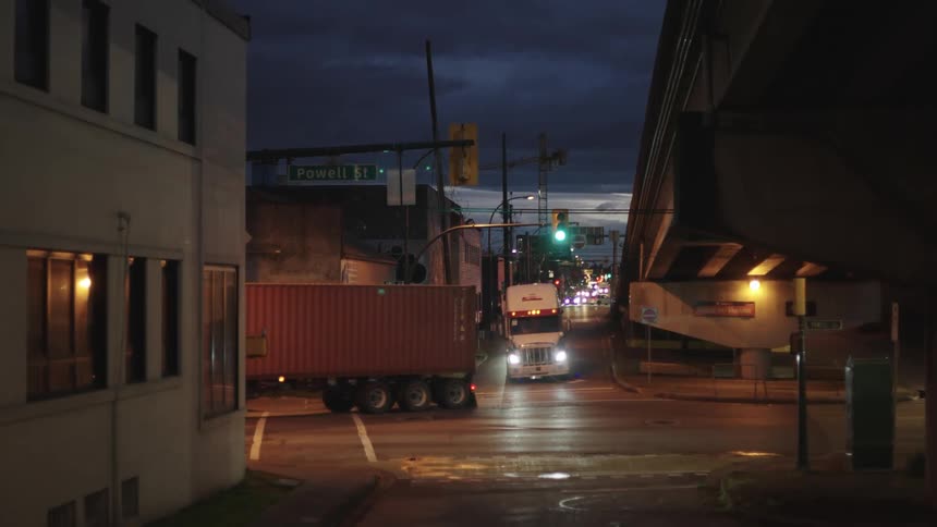 Two transport trucks are turning left on a street in a night city