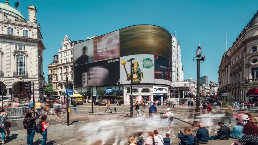 Traffic moves through plaza near stores with large outdoor digital screens displaying adverstisments