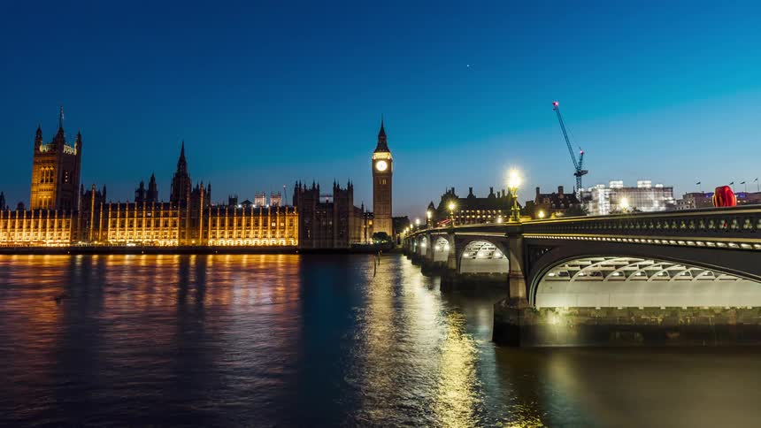 Road traffic passes over the bridge as river traffic crosses under it near the palace of westminster at night