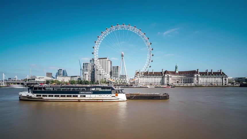 A large ferris wheel on the river front with many boats traveling nearby
