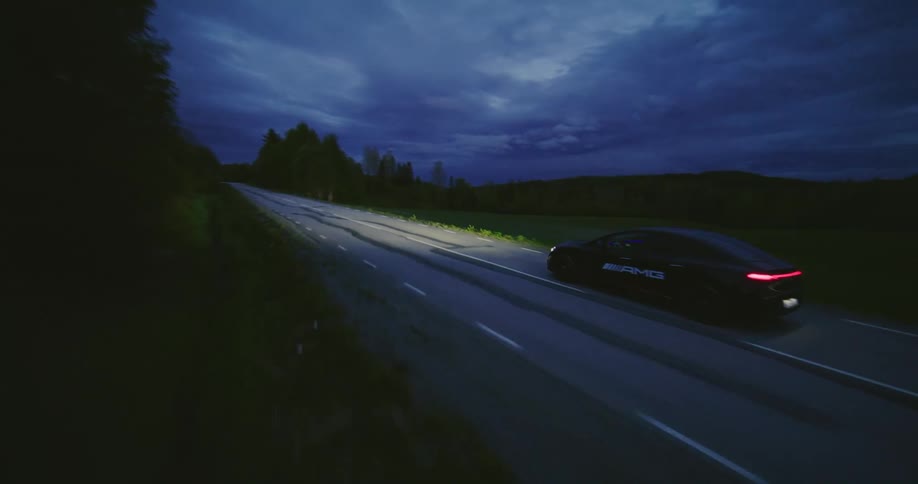Car drives along road past woods and fields on an overcast evening