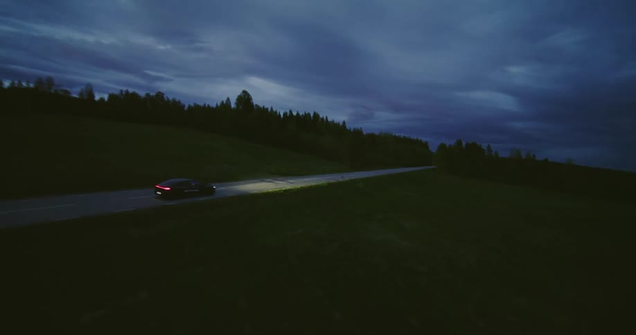 The camera swiftly pans around a sedan driving on a remote road