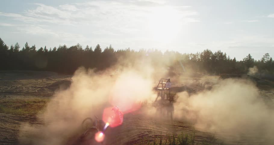 A man is sitting next to a motorcycle on a dirt track and a lot of sand smoke is in the air