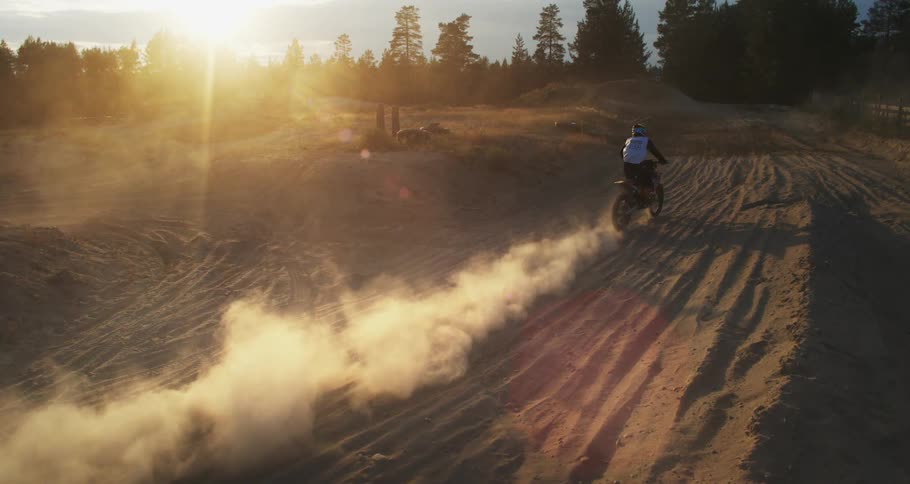 A person riding a dirt bike on a sandy track kicking up dust at sunset