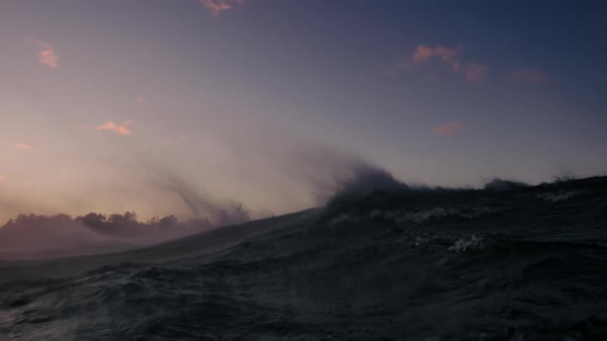 Water sprays into the air from rough off shore waves under a red tinted horizon