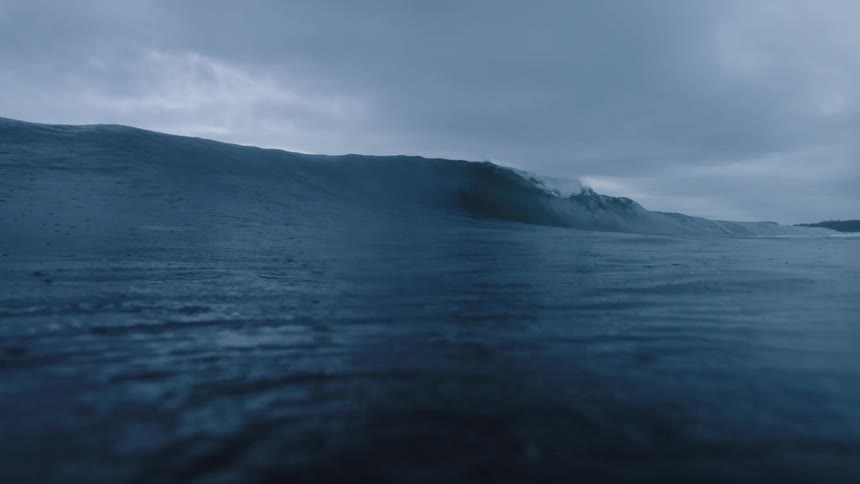A powerful wave in the ocean under a cloudy sky
