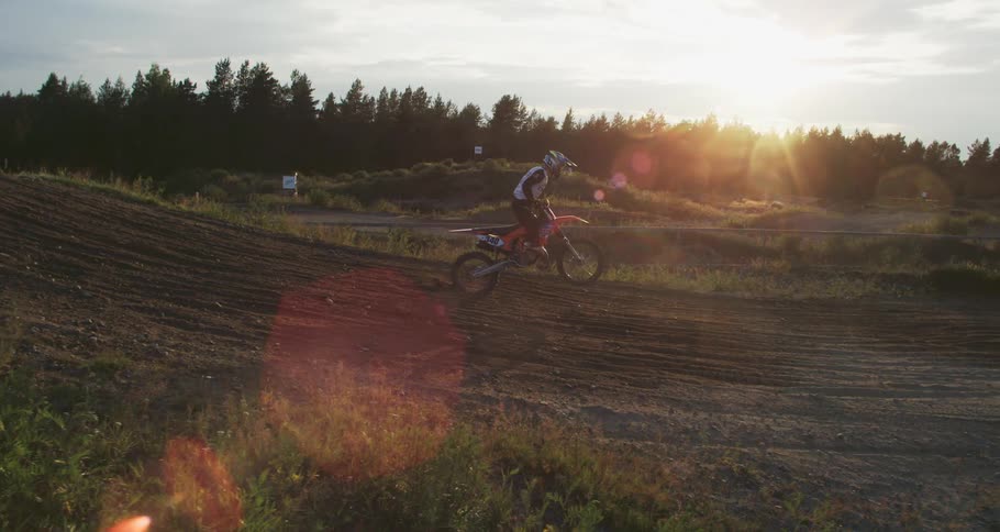 Against the backdrop of a vibrant sunset a biker donned in a helmet and a jersey shirt takes a daring leap off a hill embodying the spirit of adventure in the fading light