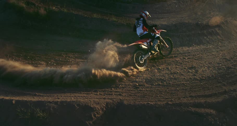 A motocross racer sliding his motorcycle sideways on a dirt track kicking up a cloud of dust