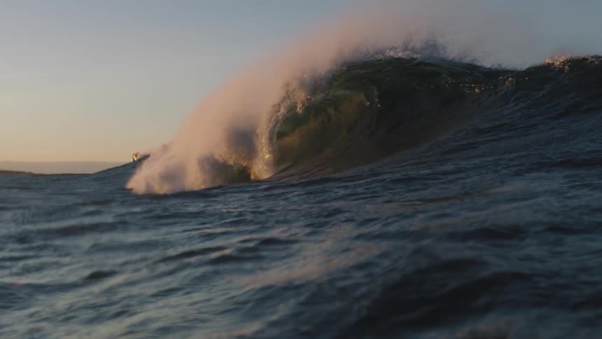 A powerful wave in the ocean under a clear sky at sunset