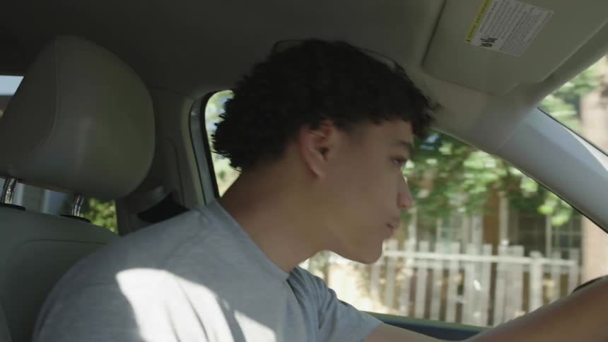 A young man drives through a neighborhood while looking around