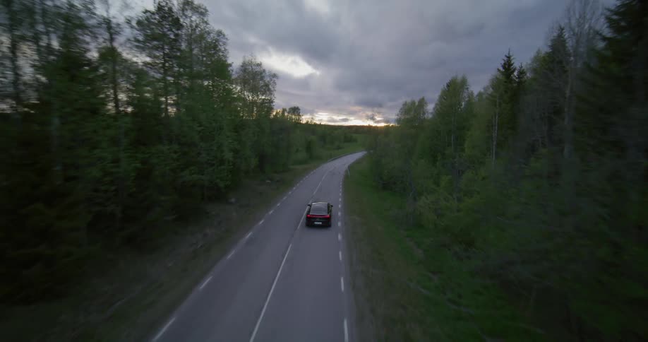 Aerial panorama of a black car driving on a highway surrounded by conifers in the morning