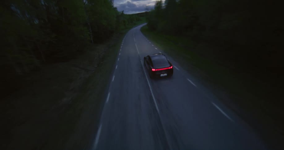 Aerial view of a black sports car driving on a country road near a forest