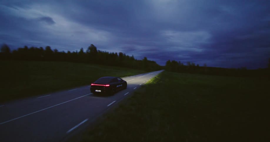 A car speeding on a road crossing the woods at night