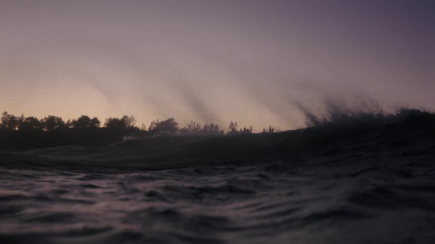 View from inside the sea with a slowmotion wave on a day with a purple sunrise sky
