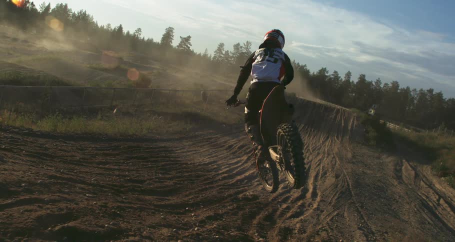 A person doing motocross jumping over a dirt ramp and doing tricks in the air