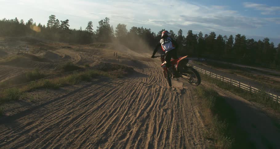 A person riding a dirt bike on a sandy track kicking up dust at sunset