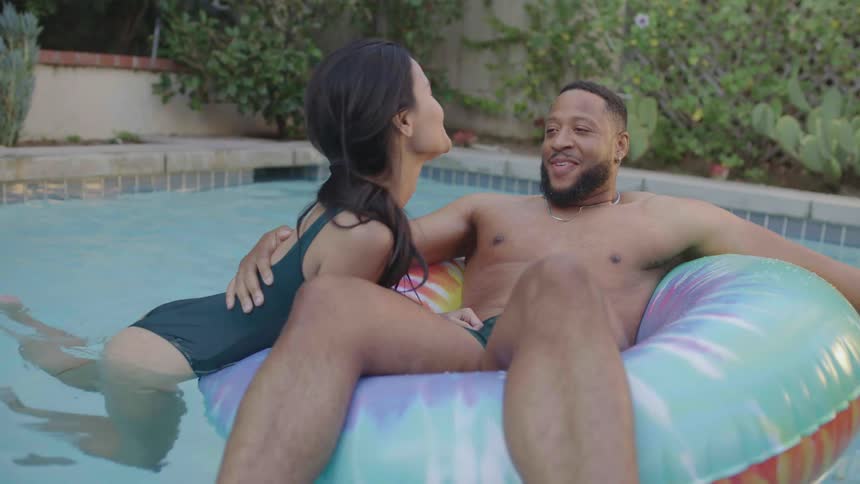 A couple in the pool where the man is on a float and the woman is pushing him