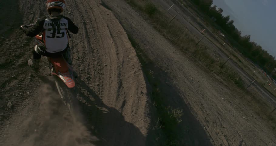 A person riding a dirt bike on a sandy track kicking up dust