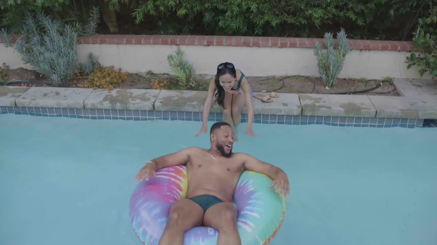 A woman at the edge of the pool pushes a man who is on a float in the water