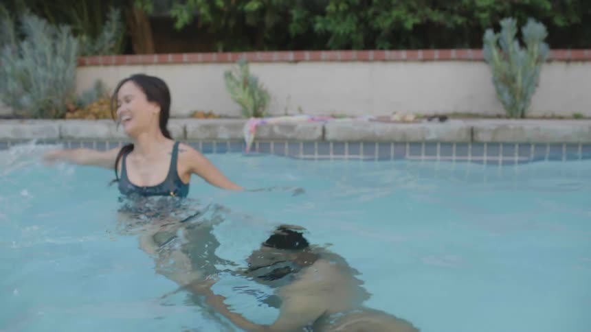 A woman playfully dunks a man in a pool and they both smile