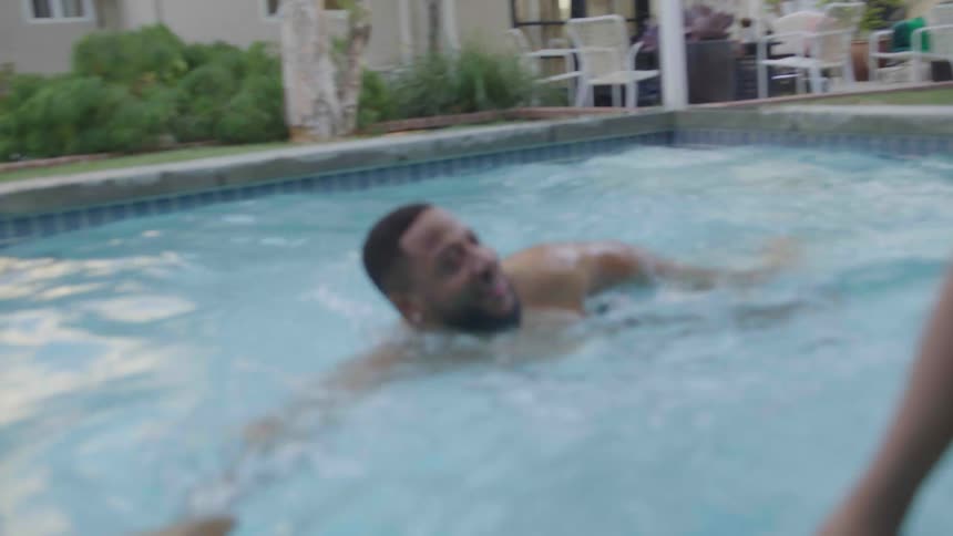 Man swimming in the pool with a woman sitting on the edge