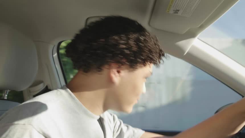 A young boy is driving a car and moving his head