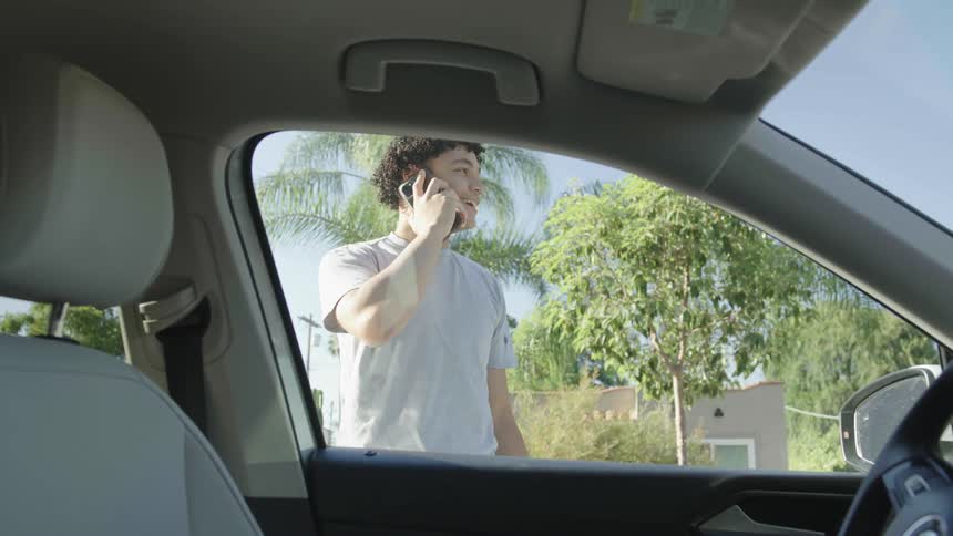 A young man gets out of the car and starts talking on his cell phone