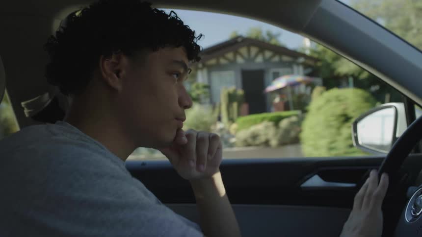 Young man driving a vehicle with one of his hands on his face