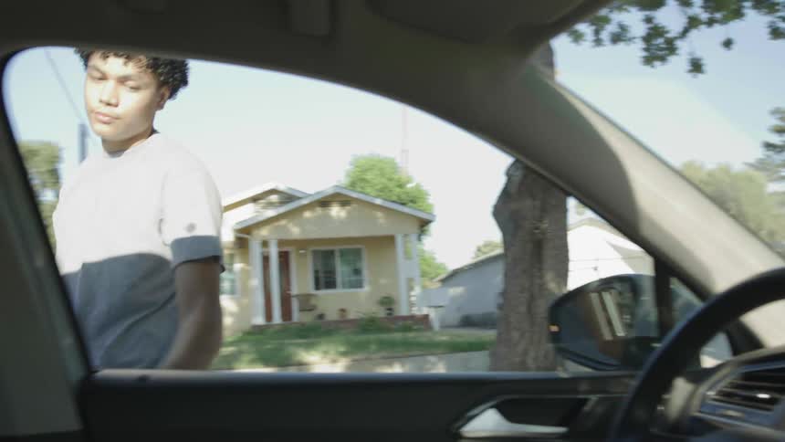 Young man walks rom the sidewalk into his car to drive off
