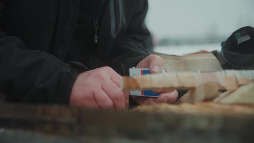 Closeup of a mans hands lighting a fire with a match in the midst of a natural location covered in snow