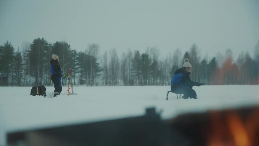 Women ice fishing on a lake next to a campfire