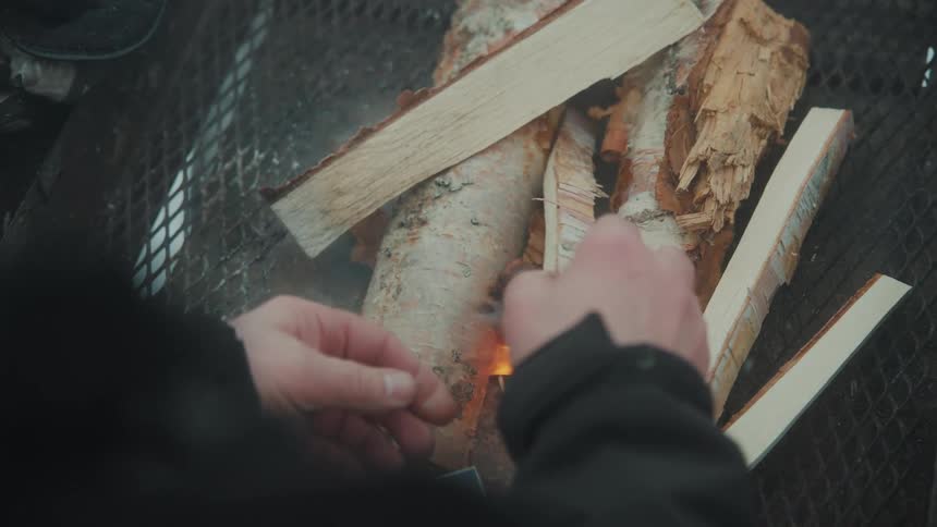 Closeup of a persons hands placing firewood into a fire