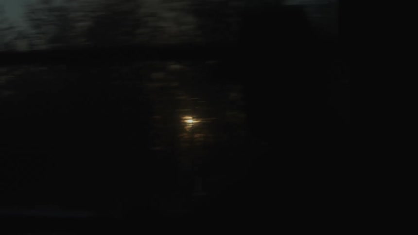 Man wearing a cowboy hat travels by train passing by a forest at sunset