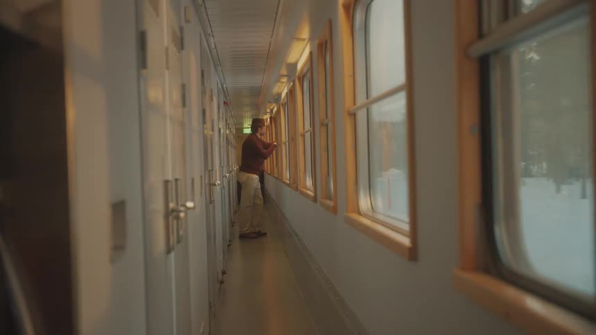 Man standing on the corridor of a train car looking out the window