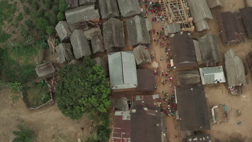 Several people are walking on a dirt road among houses in a developing country