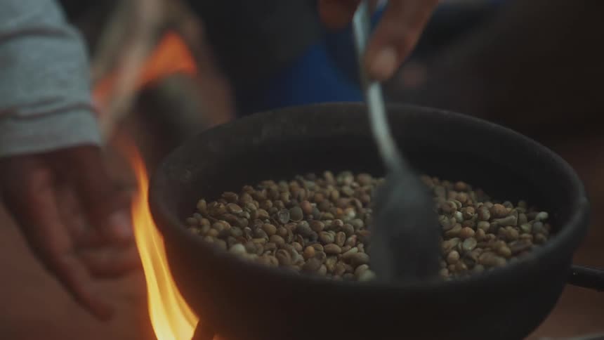 A person cooking coffee outdoors on a wood stove