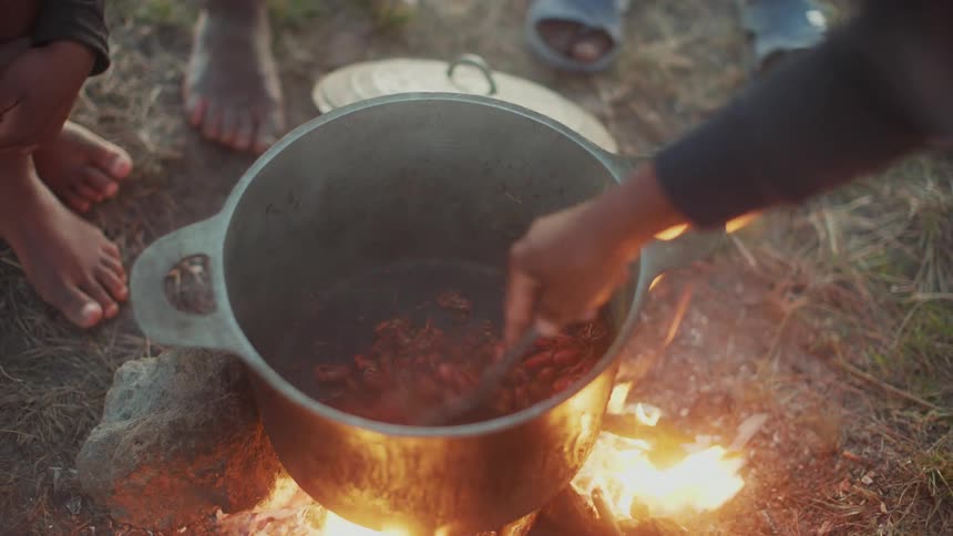 A group of people cook beef in a saucepan on a bonfire outdoors