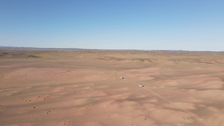 Two vehicles drive across desert sands on a clear day